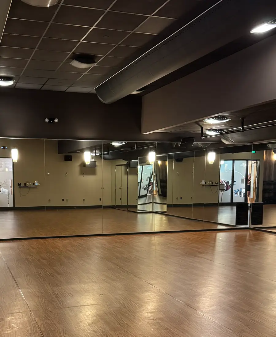 A calm open practice studio with wooden floor and mirrored wall
